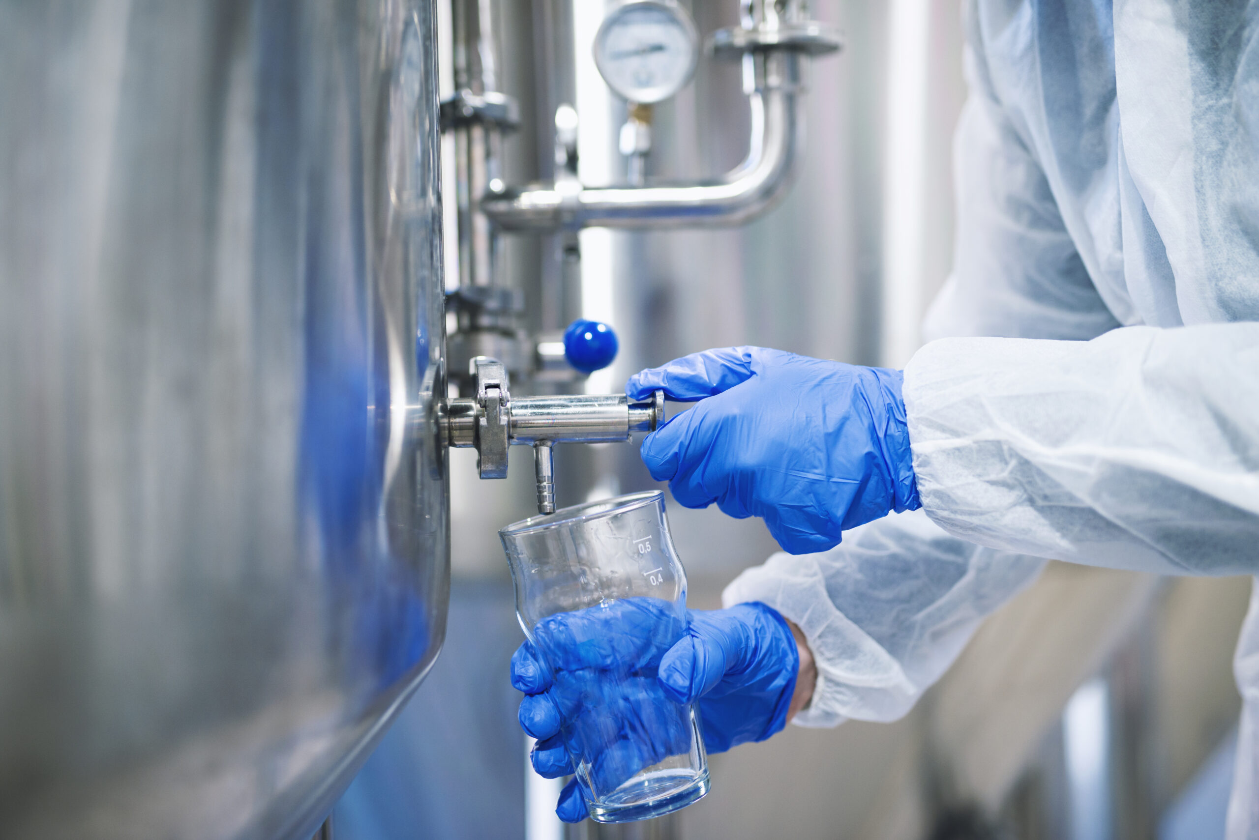 close up view hands protective gloves opening tap valve filling glass with samples from industrial machine reservoir scaled